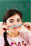 Girl holding Pencil Crayon under her Nose in Classroom