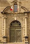 ornate facade with France flags, pillars, and wooden door on Porterie de l'abbaye in the small medieval village of Saint-Antoine-l'Abbaye, France