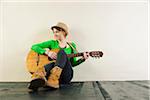 Portrait of Teenage Girl Sitting on Floor, Wearing Hat and Playing Acoustic Guitar, Studio Shot on White Background