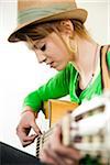 Close-up Portrait of Teenage Girl Wearing Hat and Playing Acoustic Guitar, Studio Shot on White Background