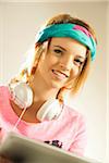 Head and shoulders portrait of teenage girl wearing a headband, headphones and using a tablet in studio.