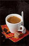 Cup of coffee with brown sugar and coffee beans on a dark background.