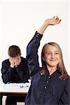 Photo of two students in class, one with a raised hand to answer a question and the other frustrated.