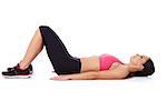 Fit young woman in gym clothes lying on her back on the floor with her knees raised exercising for health and vitality, studio portrait on white