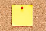 Blank yellow sticky note pined on a cork bulletin board.