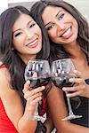 Two beautiful young women friends, Asian Chinese and Hispanic having fun drinking red wine together