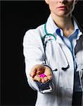 Closeup on medical doctor woman showing pills on black background