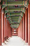 A colonnade at the Geunjeongmun Gate (or third gate) of the Gyeongbokgung Palace complex in Seoul, Korea shows the row of red columns topped by ornately painted wood beams.
