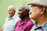 retired elderly people and free time, group of happy senior african american and caucasian male friends talking and sitting on bench in park