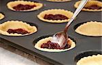 Closeup of jam tarts being filled with a metal teaspoon