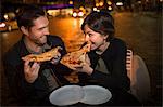 Couple eating pizza on city street