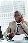 Portrait of a smiling entrepreneur making a phone call while reading a document in his office