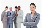 Serious saleswoman with folded arms and team behind her against a white background