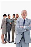 Mature businessman with arms folded and colleagues behind him against a white background