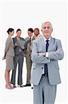 Mature businessman with arms folded and team behind him against a white background