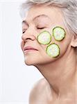 Elderly woman with a mask of cucumber on white background