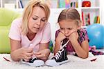 Mother teaching little unhappy girl to tie her shoes showing the process