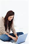 A woman smiling as she looks at her laptop with her legs crossed on the bed