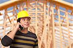 Handsome Hispanic Male Contractor on Phone in Front of New House Framing.