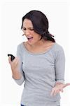 Close up of woman yelling into her mobile phone against a white background