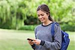 Smiling teenage girl receiving a text with her cellphone while standing in a park