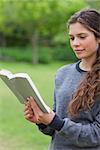 Young relaxed girl reading a book while standing upright in a park
