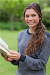 Young happy adult looking at the camera while reading a book in the countryside