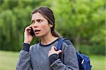 Young calm girl talking on the phone while standing in the countryside