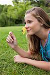 Side view of a young relaxed girl lying on the grass in a park while smelling a flower