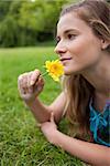 Young relaxed girl lying on the grass in the countryside while smelling a flower
