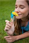Young relaxed woman smelling a beautiful yellow flower while lying on the grass