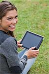 Young girl using her tablet computer while sitting on the grass and beaming