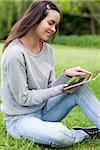 Young woman sitting on the grass in a parkland while holding a tablet computer