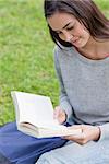 Young relaxed girl sitting on the grass in a parkland while reading a book