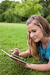Serious student lying on the grass in a park while using her tablet computer