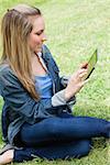 Young attractive blonde girl sitting in a park while touching her tablet computer