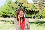 Smiling woman talking on the phone while looking toward around her in a bright grassland area
