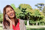 Young woman laughing joyfully while on the phone in a bright grassland  area