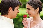 Woman smiling as she looks at her friend while holding a strawberry in a park