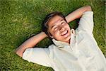 Smiling man lying with both hands resting behind his neck on the grass