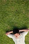 Elevated view of a man lying in grass with his eyes closed and his hands resting underneath his head