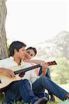 Man looking downwards while playing the guitar as his friend watches him