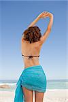 Rear view of a beautiful woman in beachwear raising and crossing her hands
