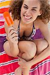 Young smiling woman placing her arms around her legs while sitting on the beach