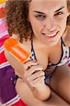 Beautiful and smiling woman in bikini holding an ice lolly while looking at the camera