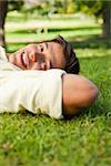Man smiling while lying in grass with his hands resting underneath the side of his head