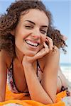 Smiling attractive woman lying on the beach with her hand on her cheek