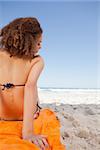 Rear view of a young beautiful woman sitting on an orange beach towel