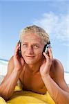 Smiling young man lying on the beach while listening to music in his headset