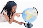 A young smiling girl is pointing at a globe against a white background